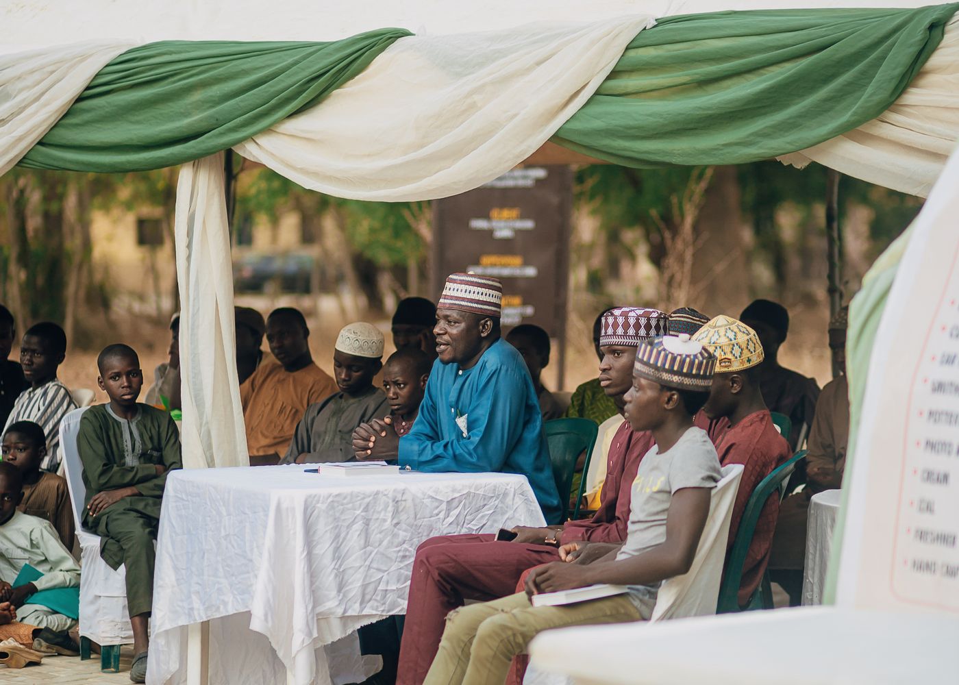 People seated beneath a canopy at an outdoor community event