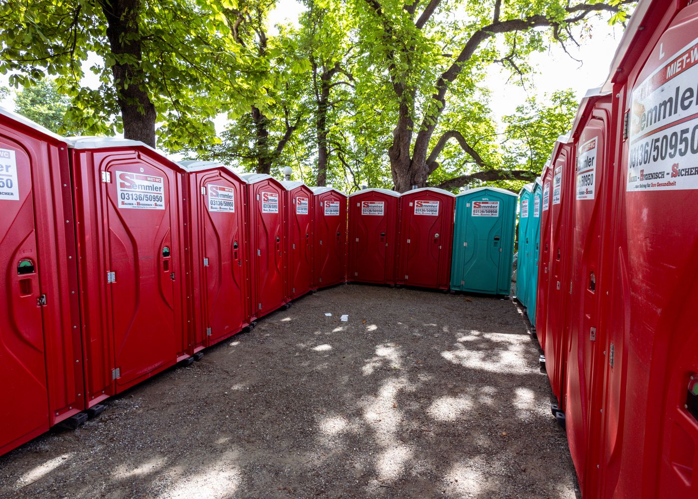 A row of red portable toilets under leafy trees